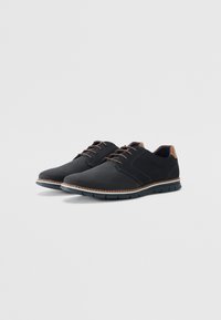 Zapatillas negras de malla y ante, con cordones marrones, un acento en marrón claro en el talón y una suela de goma flexible.