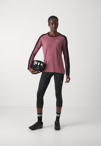 Hosszú ujjú bordó felső fekete részletekkel, fekete 3/4-es leggings és kerékpáros cipők. Fekete sisakot tart. Egyszerű dizájn, sportos szabás.