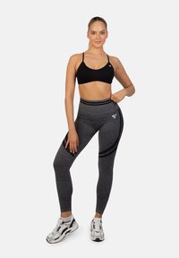 Czarny biustonosz sportowy z cienkimi ramiączkami w zestawie z wysokimi szarymi legginsami z akcentującymi paskami i teksturowanym materiałem. W komplecie białe sneakersy.