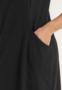 Svart klänning i mjukt tyg med en sidficka. Designen har en ren skärning och en avslappnad passform utan synliga mönster.