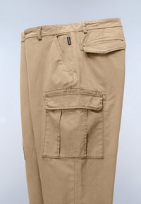 Beige cargo pants with multiple flap pockets and belt loops, shown from the side against a plain background.