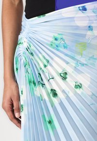 Pleated skirt in light blue fabric featuring green and white floral patterns. The texture is smooth, with vertical pleats creating dimension.