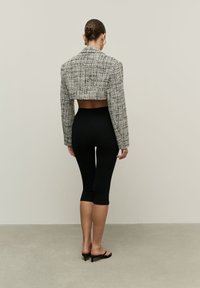 Juodai baltas trumpas tweed švarkas, derinamas su siaurais juodais leggingais ir juodomis atvirų pirštų sandalais, pabrėžiantis minimalistinį dizainą.