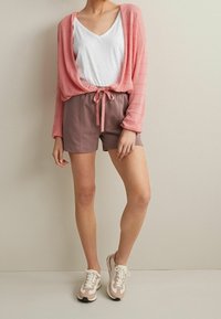 Cardigan rosa claro de manga larga, camiseta blanca de cuello en V, pantalones cortos beiges con cordón y zapatillas rosas con detalles blancos. Texturas suaves visibles.