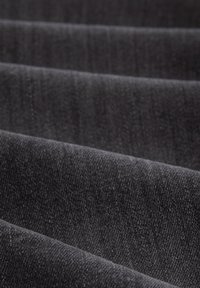 Zwarte denimstof met een zachte textuur, voorzien van een lichte glans, gevouwen in golven, met een diagonale weefpatroon en subtiele kleurvariaties.
