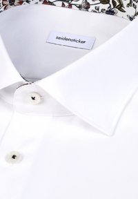 Chemise blanche boutonnée avec un col net, dotée d'un col intérieur à motif. Comprend une étiquette portant la mention « seidensticker » et un bouton noir en guise d'accent.