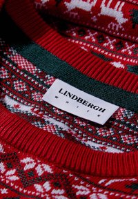 Röd tröja med ett Fair Isle-mönster i vitt och grönt, med en ribbad krage. Etiketterna säger "LINDBERGH" och "WHITE."