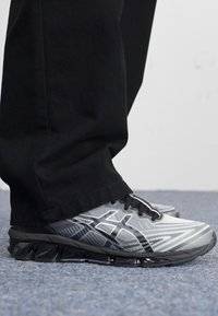 Scarpe da ginnastica grigie con accenti neri, caratterizzate da una superficie strutturata, un motivo dinamico e una suola segmentata per flessibilità.