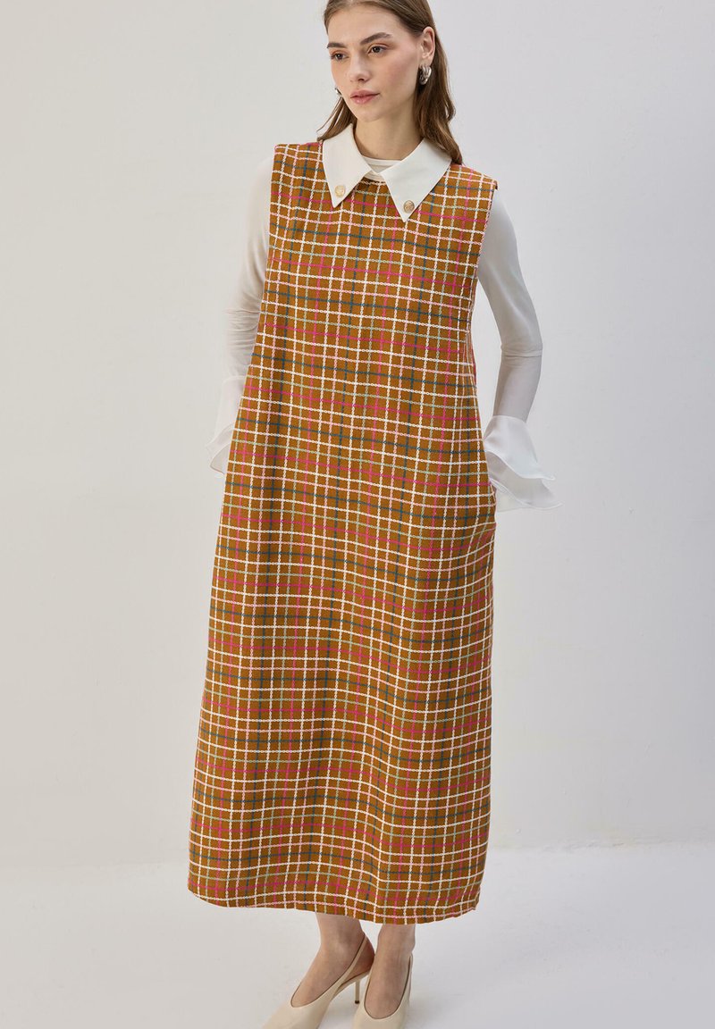 Robe à carreaux marron avec un col, présentant des accents rouges et blancs. Coupe ample, longueur aux genoux, faite en tissu texturé avec des poches.