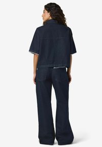 Temno modra kratka jopič z raztrganim robom in čipkastimi detajli, s kratkimi rokavi. Kombiniran z visokim pasom in širokimi hlačnicami kavbojk v ujemajočem se tkanju.