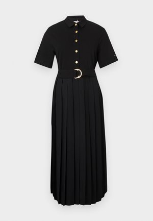 Vestido negro de manga corta, con botones en la parte delantera, falda plisada y un cinturón ancho con una hebilla redonda dorada. Tela lisa, con detalles mínimos.