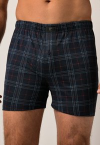 Boxers à carreaux noirs avec des motifs à rayures bleues et rouges, taille élastique et fermeture à un bouton. Fabriqués en coton.
