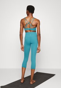 Sutiã desportivo teal com alças cruzadas e leggings de cintura alta combinando. O material parece suave e elástico com detalhes mínimos.