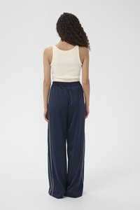 Marineblauwe satijnen broek met brede pijpen en witte zijstrepen, gecombineerd met een aansluitende geribbelde crèmekleurige tanktop. Gladde textuur en elastische tailleband.