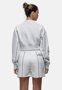 Biały krótki sweter z długimi rękawami, z detalicznym haftem, oraz pasujące białe szorty z elastycznym pasem i wzorem logo.