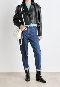 Giacca corta in pelle nera con dettagli in argento, maglione di maglia azzurro chiaro, jeans blu a vita alta, stivaletti neri e borsa bianca con coulisse.