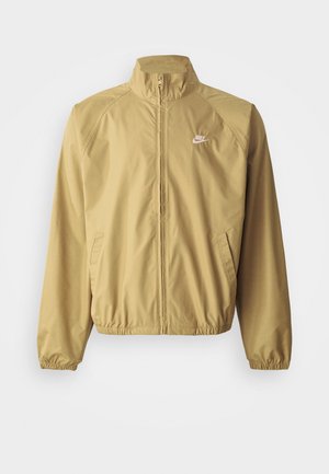 Light tan windbreaker jacket with a stand collar, full zipper, elastic cuffs, side pockets, and a small white logo on the chest.
