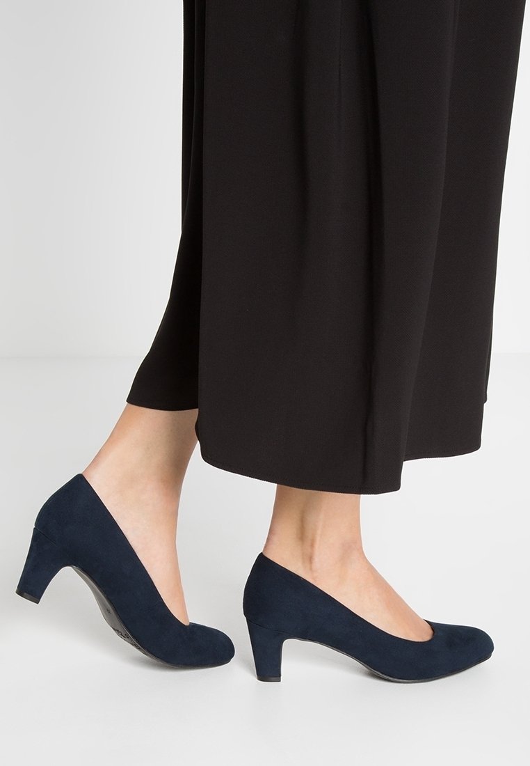 Escarpins en daim bleu marine à talons hauts avec un bout arrondi et un petit talon bloc, portés avec un pantalon noir à jambes larges. Texture lisse, design simple.