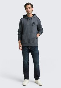 Grijze hoodie van een gestructureerde stof, met een voorkantzak en koordjes. Gecombineerd met donkere jeans en witte sneakers.