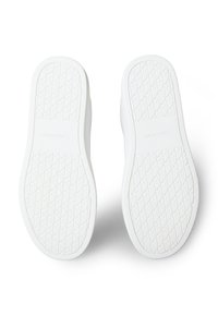 Pár bílých podrážek bot s diamantovým vzorem podrážky a raženým nápisem "Calvin Klein" uprostřed.