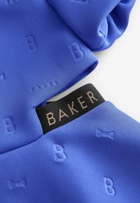 Mėlynas satinas, kurio paviršiuje yra įspausti raidės "B" raštai, su juodu žymekliu, kuriame auksinėmis raidėmis užrašyta "BAKER". Glotnus tekstūra ir blizgus paviršius.