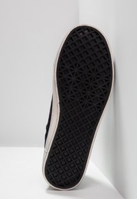 Sort sneakersål med tekstureret, diamantmønstret gummigreb. Hvid kantdetalje omkring sålen med lette slidmærker.