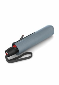 Un paraguas azul compacto guardado en una funda de tela a juego con una correa gris, que presenta un mango negro y un botón rojo de funcionamiento.