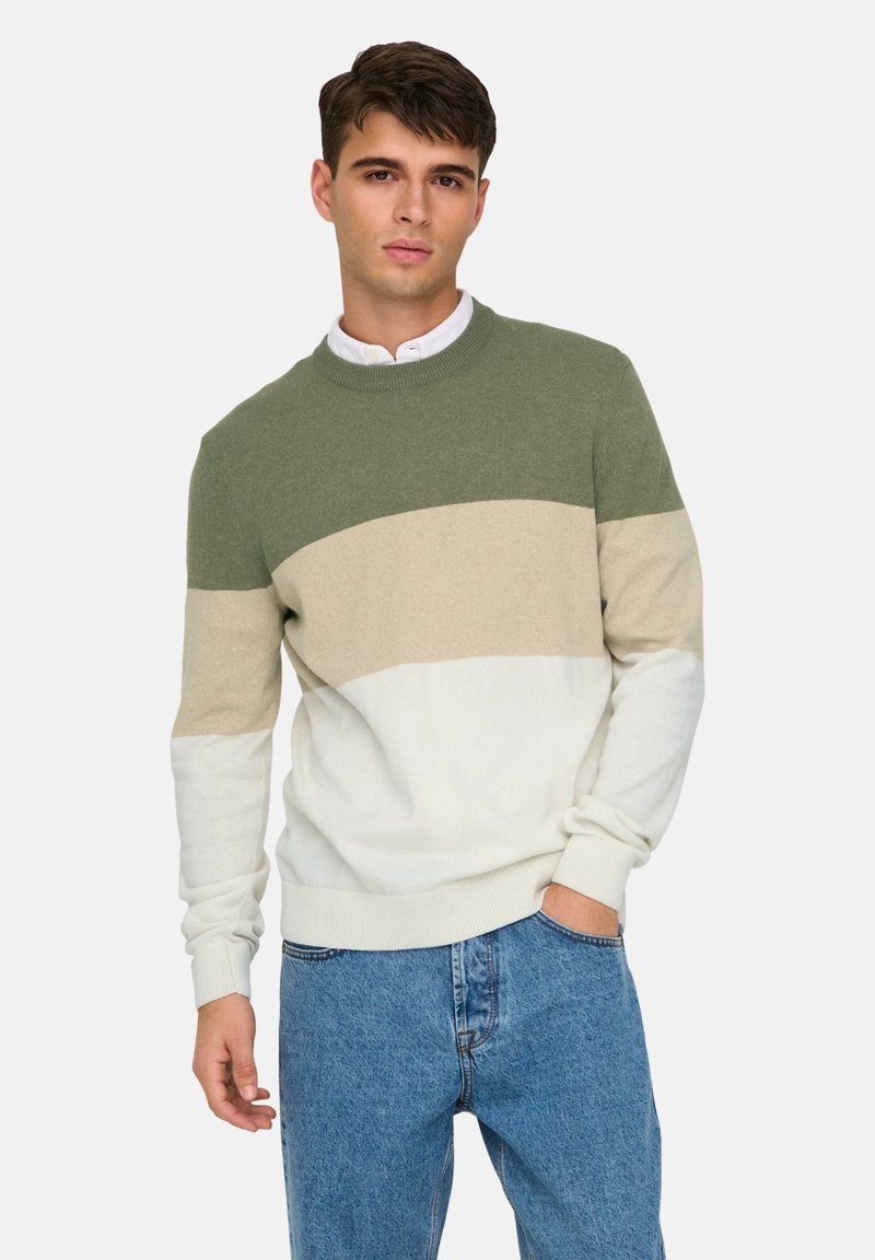 Pull en tricot avec des rayures horizontales vertes, beiges et blanches, col rond et poignets côtelés, associé à un jean en denim bleu.