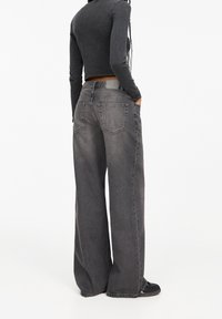 Grijze denim wijde jeans met een hoge taille, grote achterzakken en een vervaagde afwerking. Gecombineerd met een zwart langemouwen top.