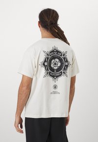 Cream-colored t-shirt with a graphic print featuring black text and a floral design on the back, short sleeves, and a relaxed fit.