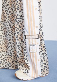 Adidas träningsbyxor med leopardsmönster i beige och svart, med vita och gyllene ränder, tryckknappar och logobrodyr.