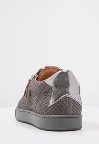Grauer, strukturierter Sneaker mit einem metallisch-silbernen Sternakzent an der Ferse und braunen Lederdetails, ausgestattet mit einer flachen Gummisohle.