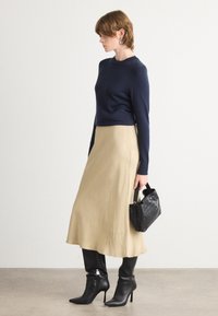 Marineblå strikket genser kombinert med en beige midinerskjørt, svarte høye støvler og en liten svart flettet håndveske. Enkel, elegant silhuett.