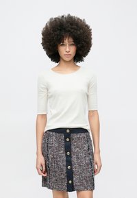 Witte, aansluitende top met korte mouwen, gecombineerd met een getextureerde, meerkleurige rok met een knoopsluiting aan de voorkant en een contrasterende tailleband.