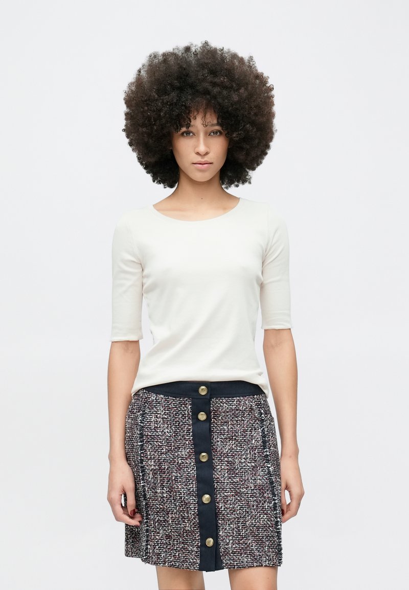 Witte, aansluitende top met korte mouwen, gecombineerd met een getextureerde, meerkleurige rok met een knoopsluiting aan de voorkant en een contrasterende tailleband.