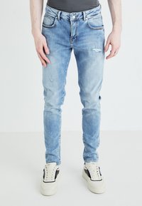 Svijetloplave skinny traperice s blagim hrapavostima, pet džepova i zatvaranjem na srebrni gumb, uparene s bijelim tenisicama.