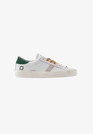 Witte lage sneaker met beige streep, groene hieltab, mosterdbotten en witte veters, en zwart vierkant logo aan de zijkant.
