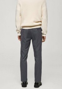 Pantaloni gri ajustați, cu o textură netedă, având un model subtil, buzunare la spate și asortați cu un pulover crem și pantofi negri.