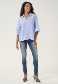 Šviesiai mėlynas ir baltas dryžuotas marškinėliai su apykakle, trumpomis rankovėmis ir laisvu pritaikymu, derinami su tamsiomis džinsais ir aukštakulniais sandalais.