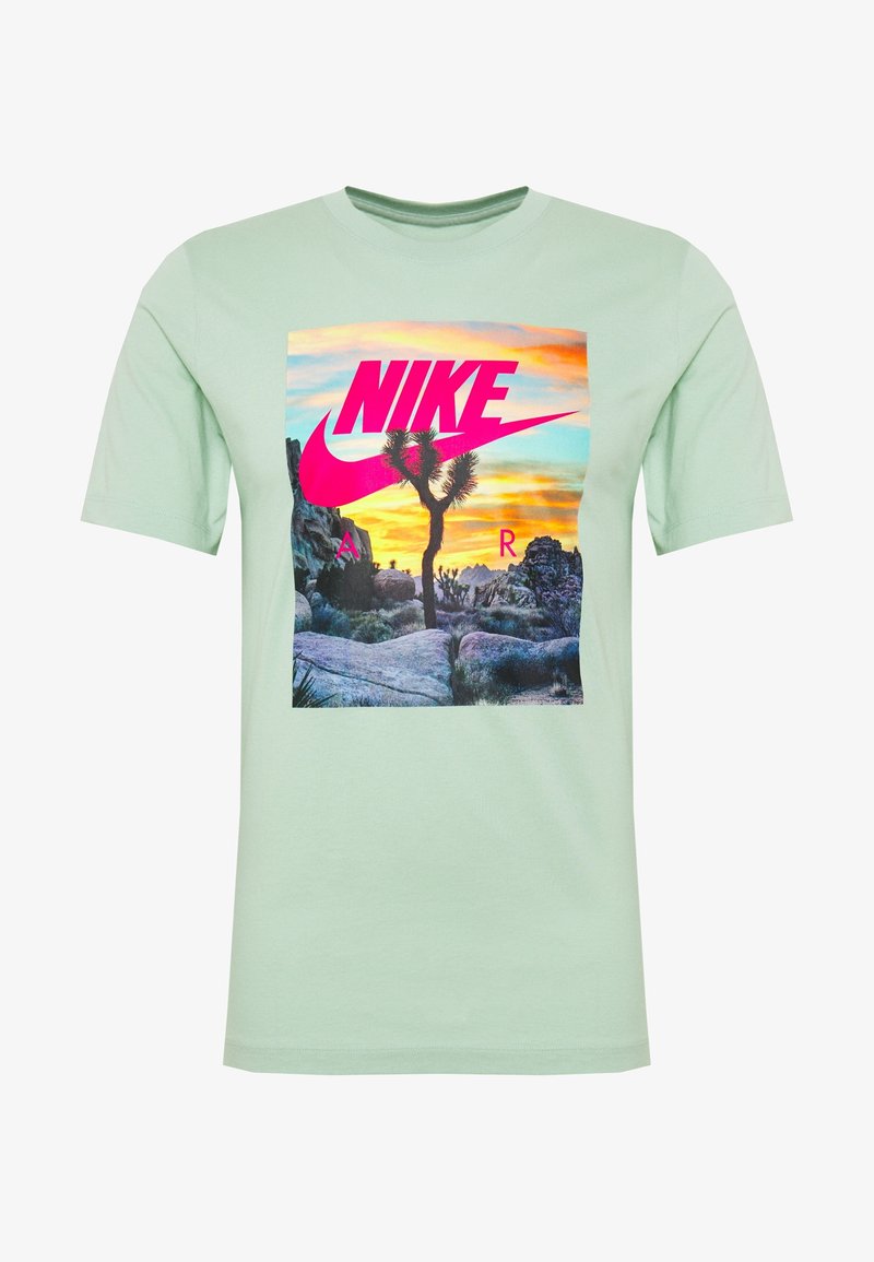 Ljusgrön bomulls-t-shirt med en grafik av ett Joshua-träd och solnedgång samt en rosa Nike-logotyp centrerad på framsidan.