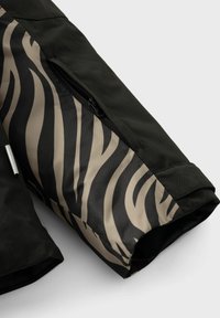 Schwarzer Jackenärmel mit einem kontrastierenden Innenfutter, das ein beiges und schwarzes Zebra-Streifenmuster aufweist, sowie einem Reißverschluss.