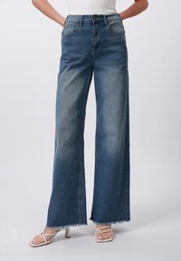 Høytlivte, vide jeans i mellomblå denim med en falmet finish og frynsete kant; fire lommer og en knappelukking.