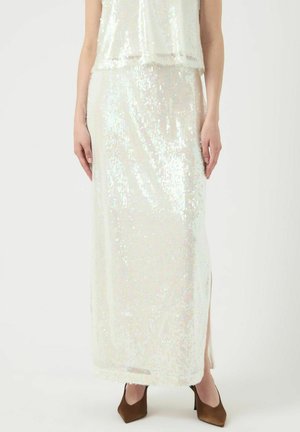 Maxi jurk en top set in iriserend paillettenmateriaal; doorschijnende overlay; zijslitsen; losse pasvorm. Bruine hoge hakken completeren de outfit.
