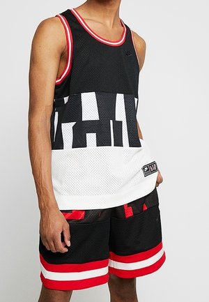 Musta verkkotoppi, jossa on suurta valkoista tekstiä, punaisia yksityiskohtia ja valkoinen alaosa; yhdistettynä mustiin shortseihin, joissa on punaisia ja valkoisia raitoja.