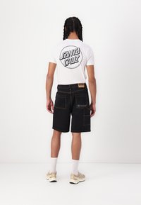 Sorte denimshorts med gule stikninger, der har to baglommer. Hvid t-shirt med et cirkulært "Santa Cruz" logo på ryggen.