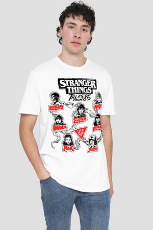 Young man wearing white Stranger Things graphic tee featuring character illustrations and names, paired with blue jeans, against plain background.