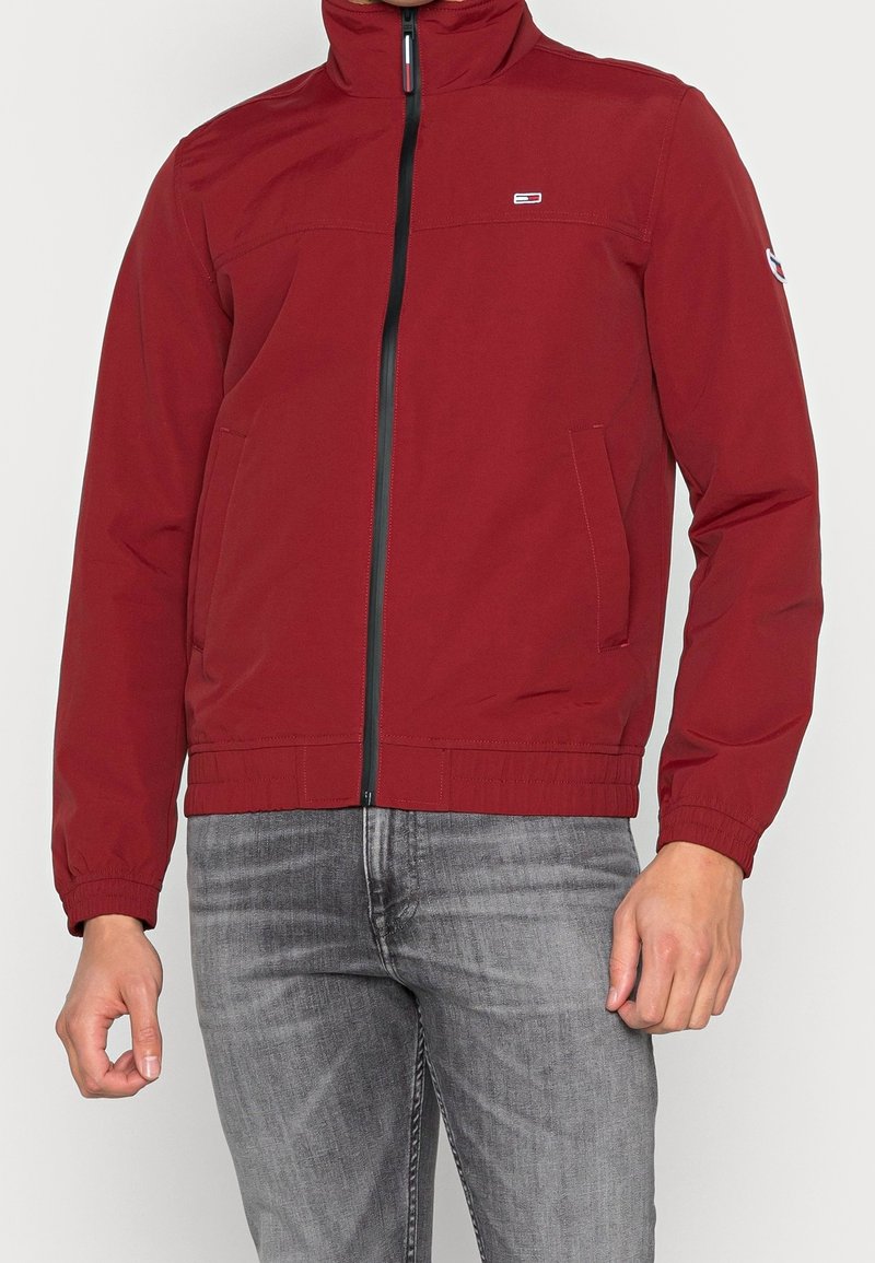 Rote, leichte Jacke mit hohem Kragen, Reißverschluss, zwei Seitentaschen und elastischen Bündchen. Mit kleinem Logo auf der Brust.