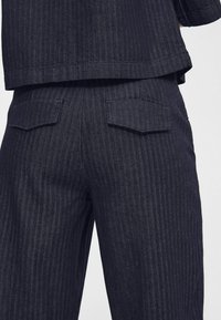 Mörk denimliknande byxor med ett fiskbensmönster, två bakfickor, något avsmalnande ben, texturerad tyg och en ren finish.