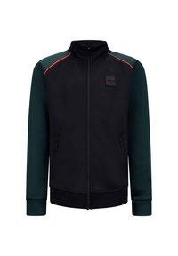 Zwarte jas met groene mouwen, rits aan de voorkant, hoge kraag en zijzakken. Heeft rode accentstiksels en een logo-patch op de borst.