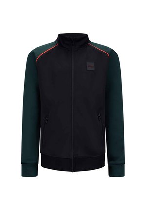 Schwarze Jacke mit grünen Ärmeln, mit Reißverschluss vorne, hohem Kragen und Seitentaschen. Mit roten Akzenten und einem Logo-Patch auf der Brust.